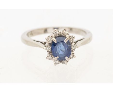 A sapphire and diamond white metal cluster ring, comprising a claw set oval mixed cut sapphire, approx 6 x 4mm, within a bord