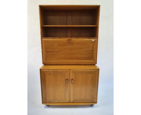 An Ercol light elm cabinet, with open shelf above fall front to reveal a fitted interior on a base with two cupboard doors, 9