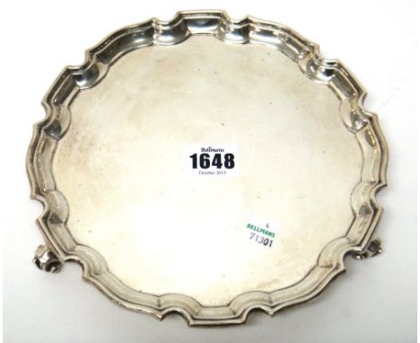 A silver salver, of shaped circular form, decorated with a piecrust rim, in a Chippendale style and raised on three scrolling