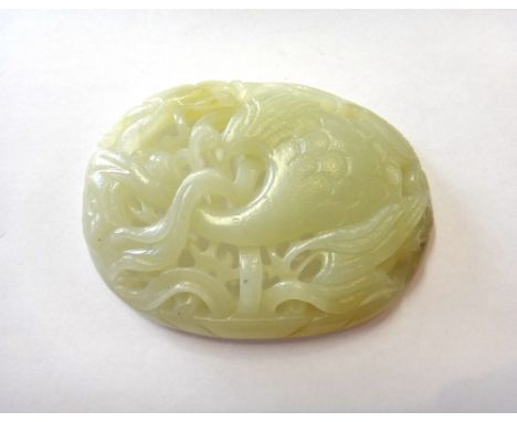 A Chinese jade oval plaque, carved and pierced with a crane in flight amongst lotus, the stone of a pale celadon tone with so