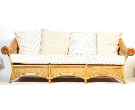 A contemporary three seater cane bamboo wicker conservatory sofa having carved wooden circular floral elbow rests over three 