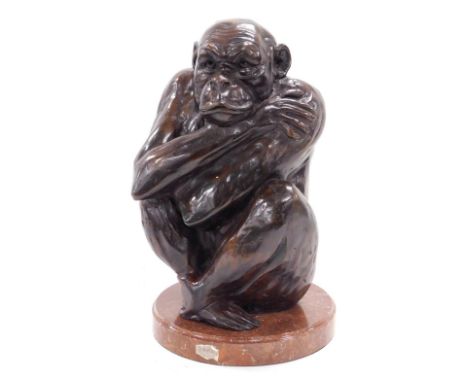 An early 20thC French bronze figure of a monkey, modelled seated with arms clasped, raised on a red porphyry marble base, 35c