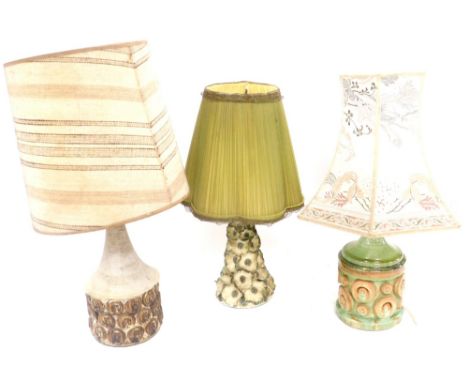 Three mid century pottery table lamps, comprising a floral encrusted lamp with a green frilled shade, 49cm high, green glazed