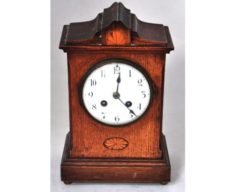 An early 20th century inlaid oak cased mantel clock with enamel dial set with Arabic numerals, 29cm.