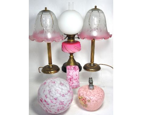 A brass and pink opaque glass oil lamp, a brass column lamp with pink floral glass shade, a pink globe mottled glass ceiling 