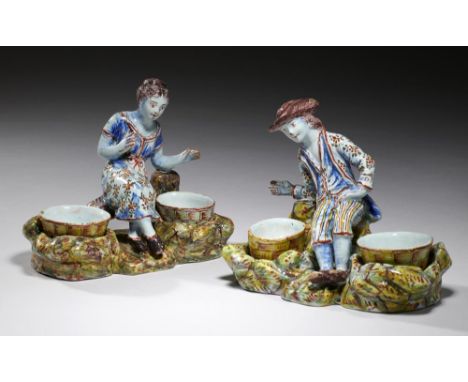 A PAIR OF DUTCH DELFTWARE FIGURAL CRUETS,  18TH/EARLY 19TH C  as a seated youth or girl, the rocky base with detachable round