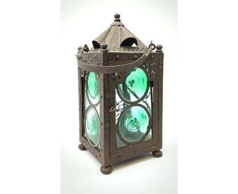 An Arts &amp; Crafts wrought iron lantern, of square sided form with swing handle, and green and clear glass panels, raised u