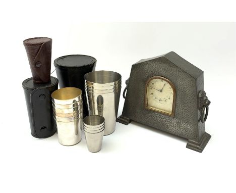 A 20th century planished pewter clock, with guilloche enamel dial, twin lion mask ring handles, and raised upon two stepped b