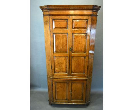 A George III Oak Standing Corner Cabinet, the moulded cornice above two moulded doors enclosing shelves, the lower section wi