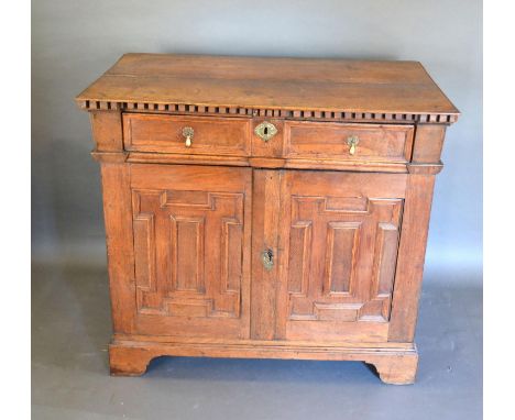 A George III Oak Side Cabinet with a frieze drawer above two geometrically moulded doors enclosing drawers with brass drop ha