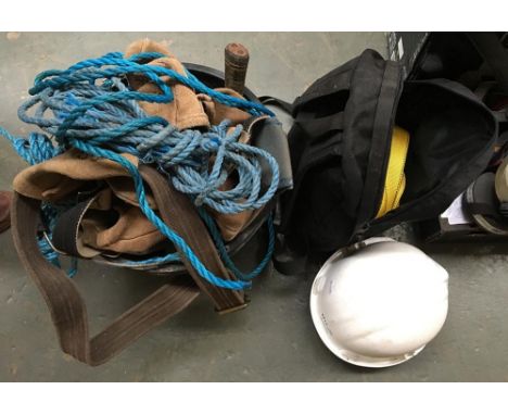 A hard hat and safety harness, together with a bucket with rope, toolbelts, hammers, and other tools 