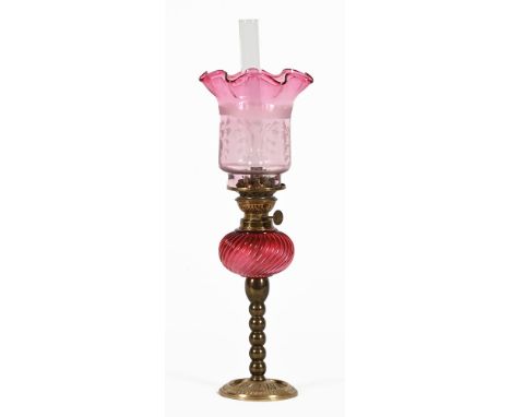 A Victorian slim line oil lamp, with red glass reservoir, etched red glass shade, kosmos burner and chimney raised on brass b