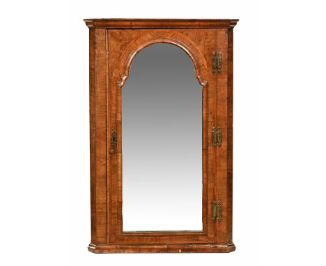 An early 18th century walnut hanging corner cupboard, the mirrored door with arched and moulded surround opening to shelves a