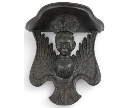 A 17th century style ebonised oak wall bracket carved as crowned angel with serpentine shelf, 32cm wide, 30cm high Dark eboni