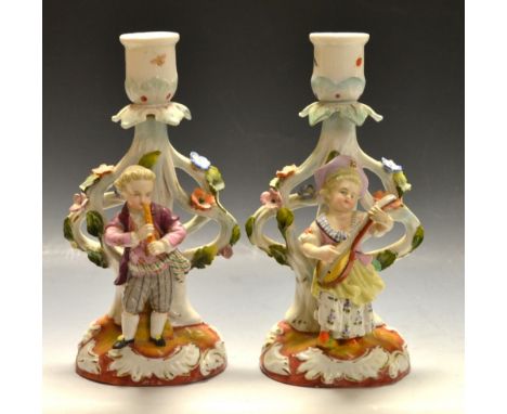 A pair of continental figural candlesticks as a girl and boy playing musical instruments, underglaze blue cross marks