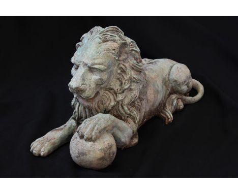 A SCULPTURAL BRONZE EFFECT HERALDIC LION, the lion recumbent with left paw resting on a ball, 25cm high, 51cm wide.