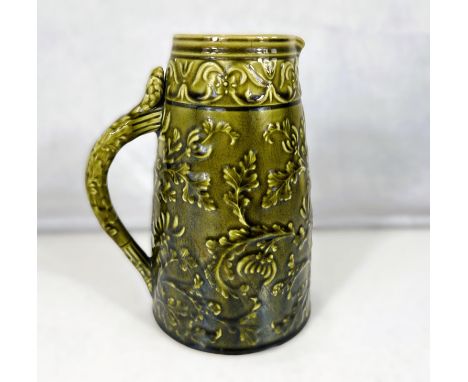 Linthorpe Art Pottery: A jug of tapering cylindrical form with relief decoration of ferns and leaves under a dark green glaze