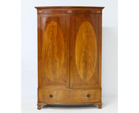 Edwardian mahogany and inlaid bow front wardrobe, having a dentil cornice with a shell inlaid frieze over two oval feathered 