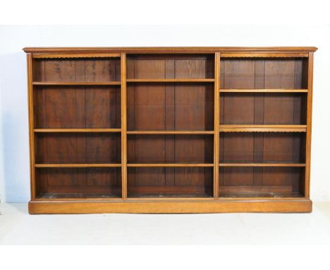 Victorian style walnut triple open bookcase, having an egg and dart carved frieze, over adjustable shelves, raised on a plint