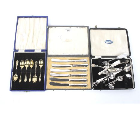 An assortment of silver and white metal flatware. Including a cased set of six butter knives, gilt teaspoons, etc