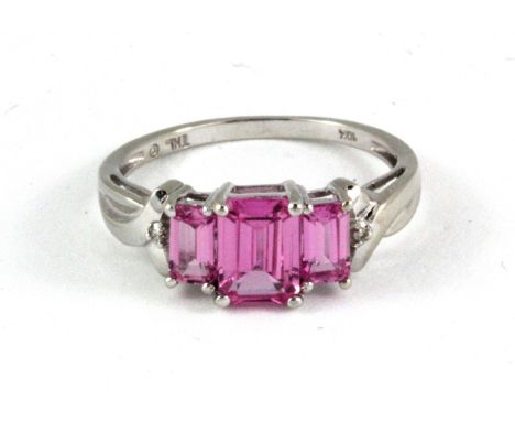 A 9ct white gold (stamped 10k) ring set with three emerald cut pink sapphires and diamond set shoulders, (N.5).