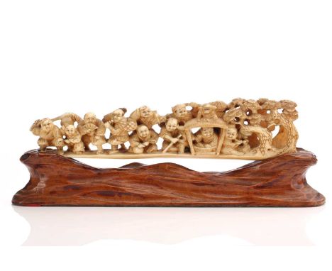 A Japanese ivory okimono, Meiji period, carved as eleven humorous figures, a monkey and a small Daruma, a group of pine trees