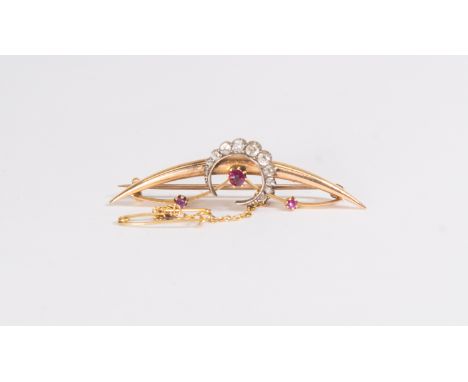 A ruby and diamond crescent brooch, comprising an unmarked yellow metal curved detail, set with two claw set rubies either si