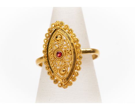 An unmarked high carat (tests as 22ct gold) ethnic design with granular decoration to the border, marquise shaped with red en