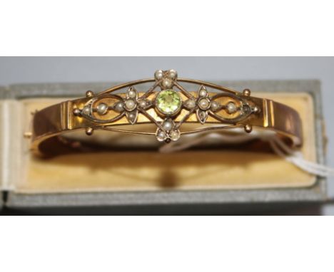 A George V 9ct gold, peridot and seed pearl set hinged bangle, in box.