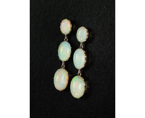 A pair of graduated opal ear pendants, each designed as three graduated oval cabochon opals claw set in white metal with post