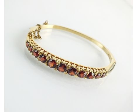 A 9ct gold graduated garnet hinged bangle, designed as eleven graduated round mixed cut garnets, all claw set in yellow gold,