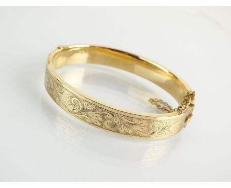 A 9ct gold hinged bangle, with bright cut engraved decoration and attached safety chain, hallmarked Birmingham 1972, weight 1