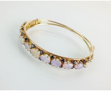 An opal and sapphire hinged bangle, designed as eleven partially graduated oval cabochon opals interspersed with twenty facet