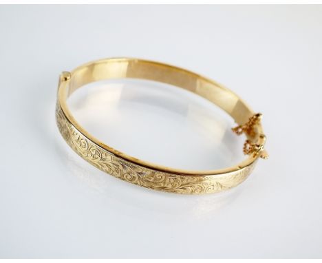 A 9ct gold hinged bangle with bright cut engraved decoration and attached safety chain, hallmarked Chester 1954, weight 9.7gm