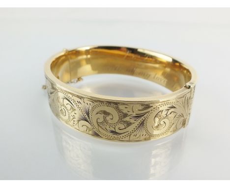A 9ct gold hinged bangle, with bright cut engraved decoration and presentation engraving to interior, attached safety chain, 