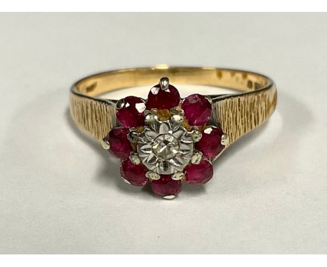 A ruby and diamond cluster ring, central round brilliant cut diamond surrounded by eight red rubies, 9ct gold textured shank,