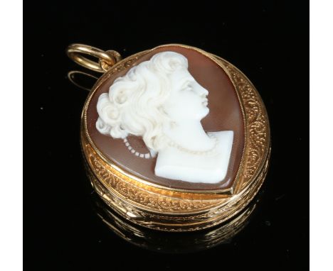 An 18 carat gold locket set with a heart shaped shell cameo portrait of a young lady. Decorated to the reverse in gold overla