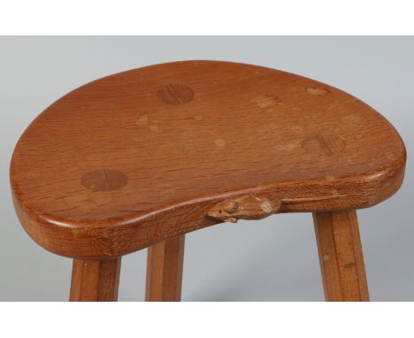 A Robert Mouseman Thompson oak three legged stool with dished kidney shaped top. Carved with the Mouseman motif to the front 