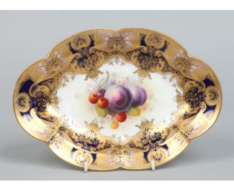 A Royal Worcester lobed oval dish by Albert Shuck. Painted with plums and cherries framed within a wide gilt, cobalt blue and