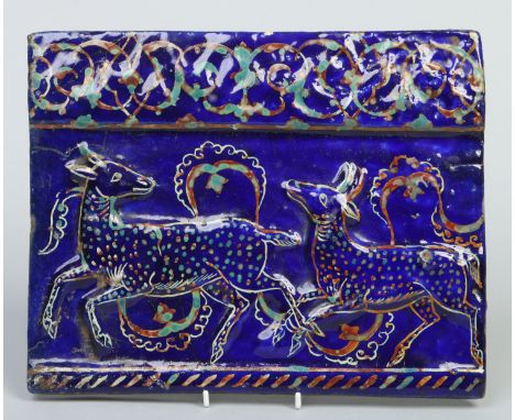 An 18th century Islamic frieze tile. Gros bleu ground and moulded in relief with two deer between iridescent scrolling border