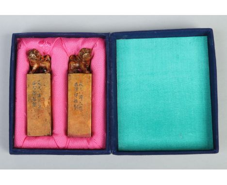 A cased pair of Chinese carved soapstone seals. Each surmounted with a dog of fo, with incised inscriptions to the sides and 