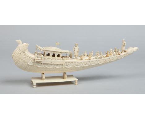 A 19th century Cantonese carved ivory model of a boat raised on a plinth and surmounted with figures, 38cm long.    Condition