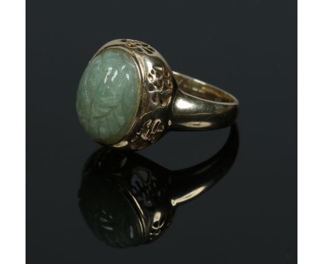 A Chinese 14 carat gold ring. Set with an ovoid celadon jade pebble, the shank pierced with six characters. Size P.   Conditi