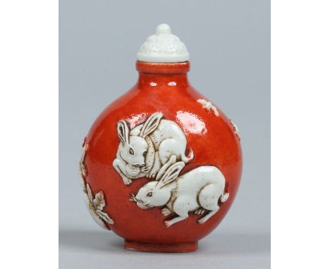 A Chinese Daoguang (1820-50) snuff bottle and cover. Ground in rouge de fer and moulded with a pair of rabbits, a radish and 