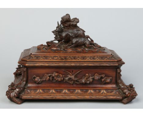 A 19th century Black Forrest carved walnut table casket of canted sarcophagus form. Surmounted with models of a dog and goat,