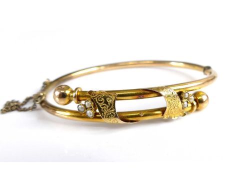 A Victorian yellow metal hollow hinge bangle, with safety chain, the crossover section united by two seed pearl set three-lea