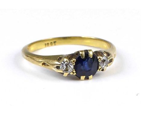 An 18ct gold sapphire and diamond three-stone ring, the centre four-claw set oval cut sapphire flanked to either side by a si