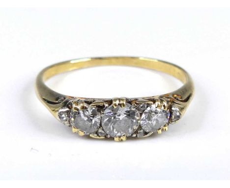 A yellow metal diamond 3 stone ring featuring 3 graduated old European cut diamonds in carved claw settings with 5 rose cut d