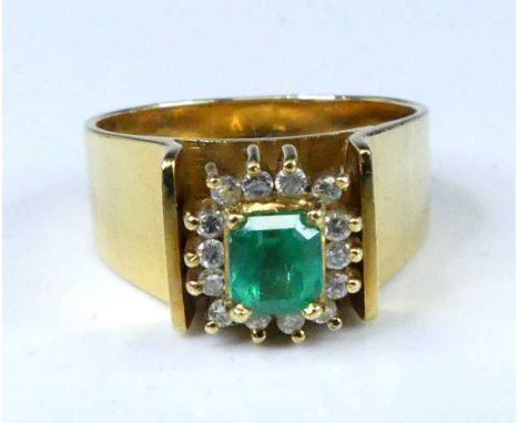 A yellow metal, emerald and diamond rectangular cluster ring, featuring an octagonal cut emerald within a border of 14 round 