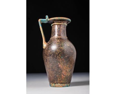 Ca. AD 200 - 300.A deep turquoise glass pitcher with brown iridescence. The vessel features a tall body with a ring base, a r